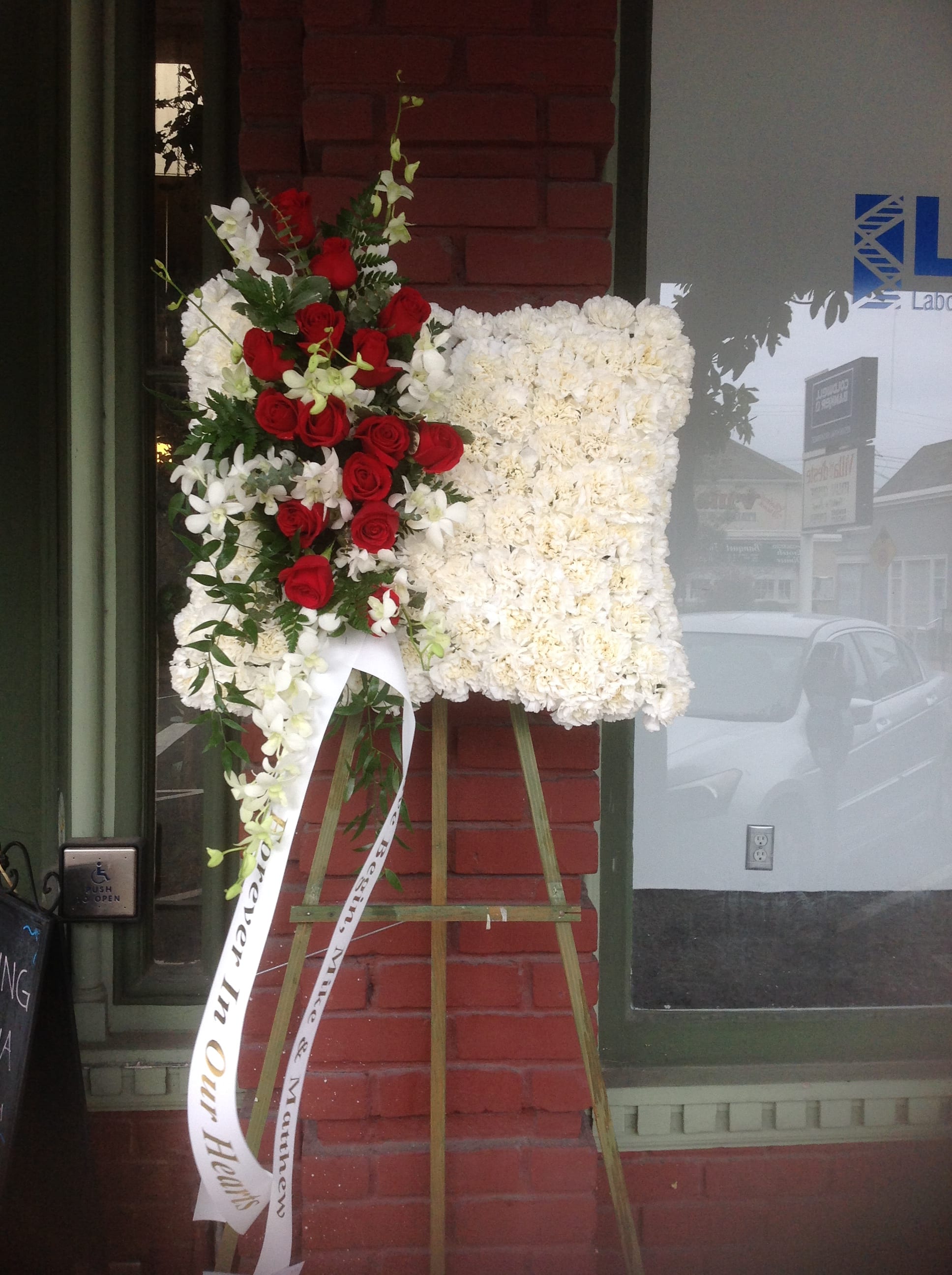 Standing floral easel with red roses and white flowers on a ribboned display