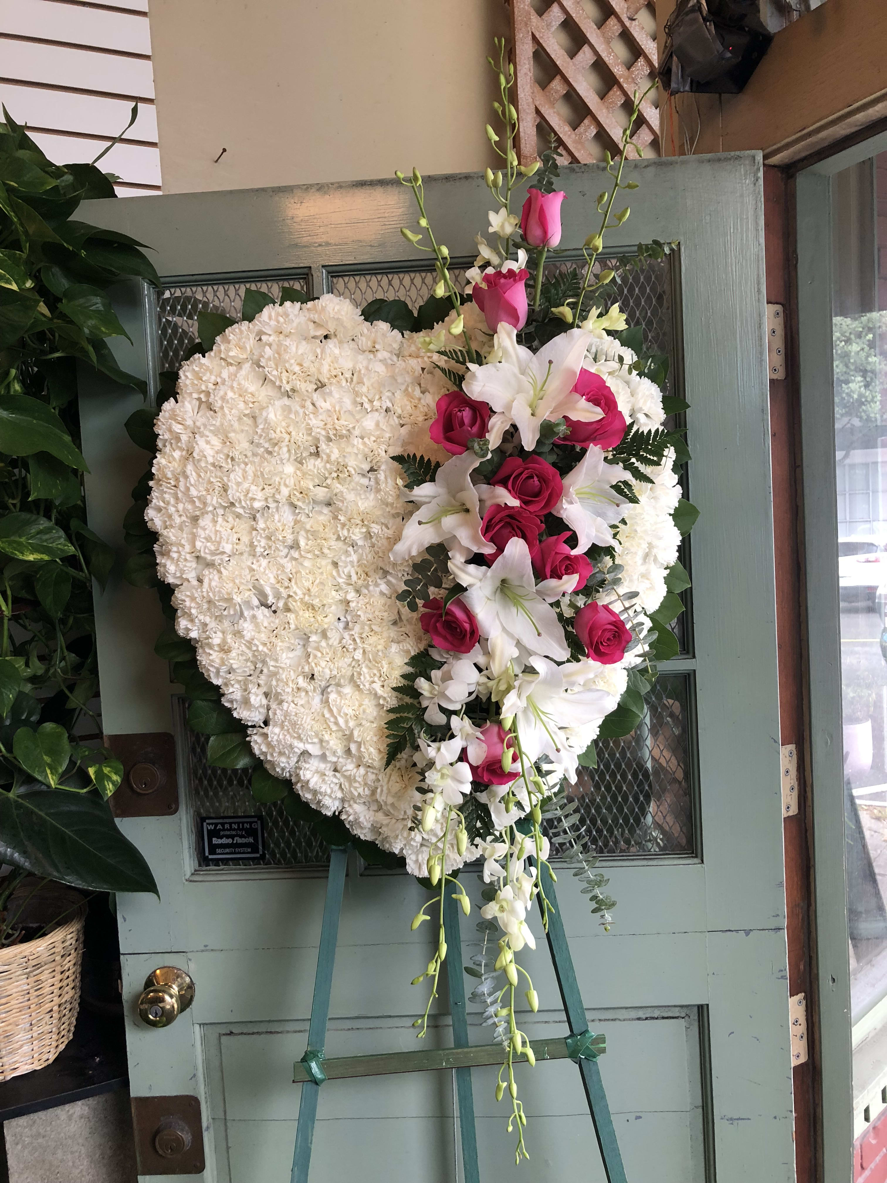 Heart-shaped white floral wreath with pink roses and lilies on an easel