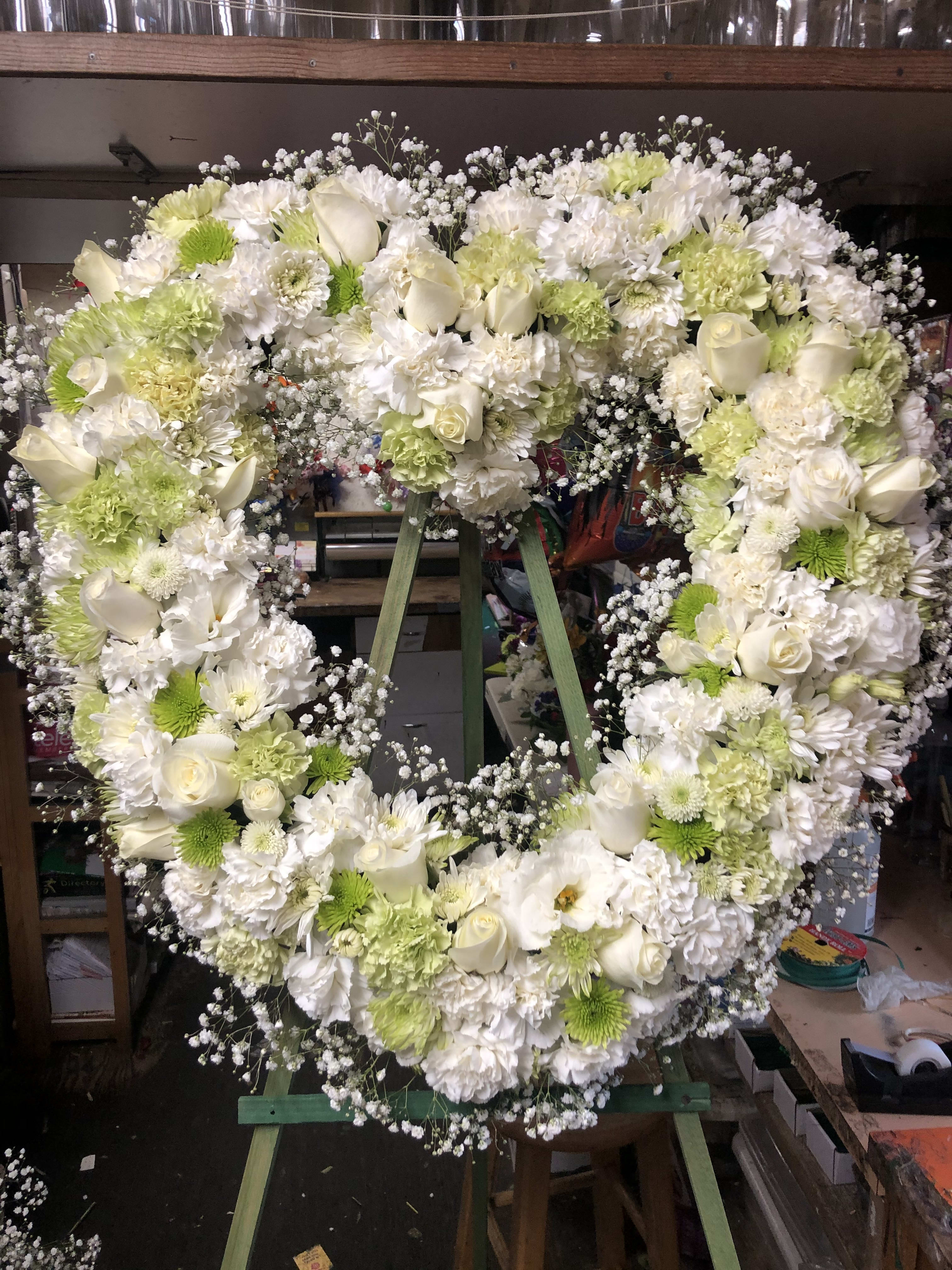 Heart-shaped floral wreath of white and pale green flowers on an easel