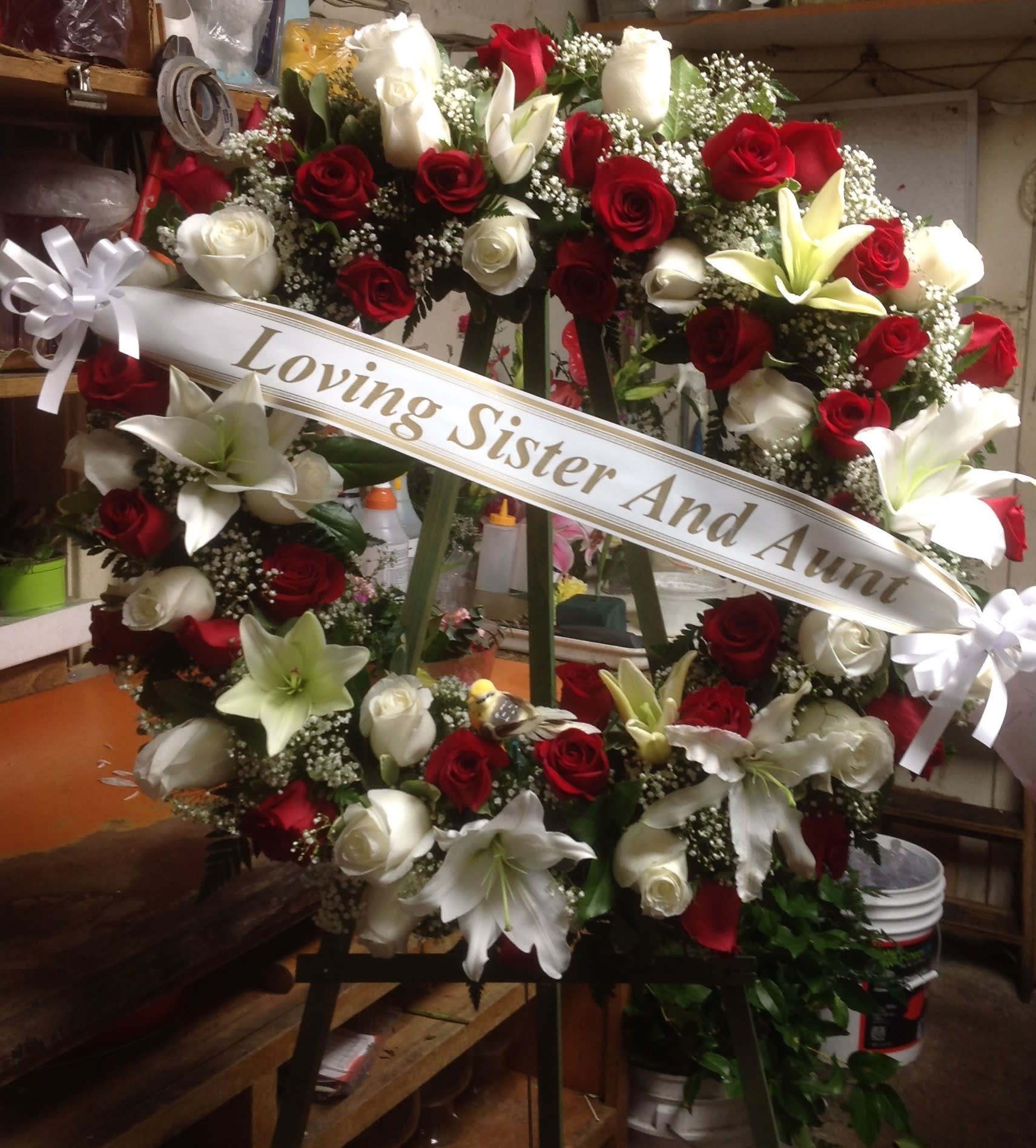 Heart-shaped wreath of red and white roses with lilies and a memorial ribbon