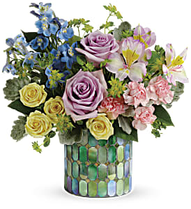 Mixed bouquet of roses, lilies, and blue flowers in a mosaic vase
