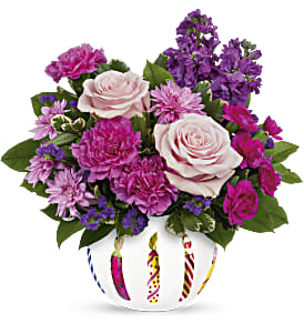 Pink and purple flower arrangement in a white vase with candle designs