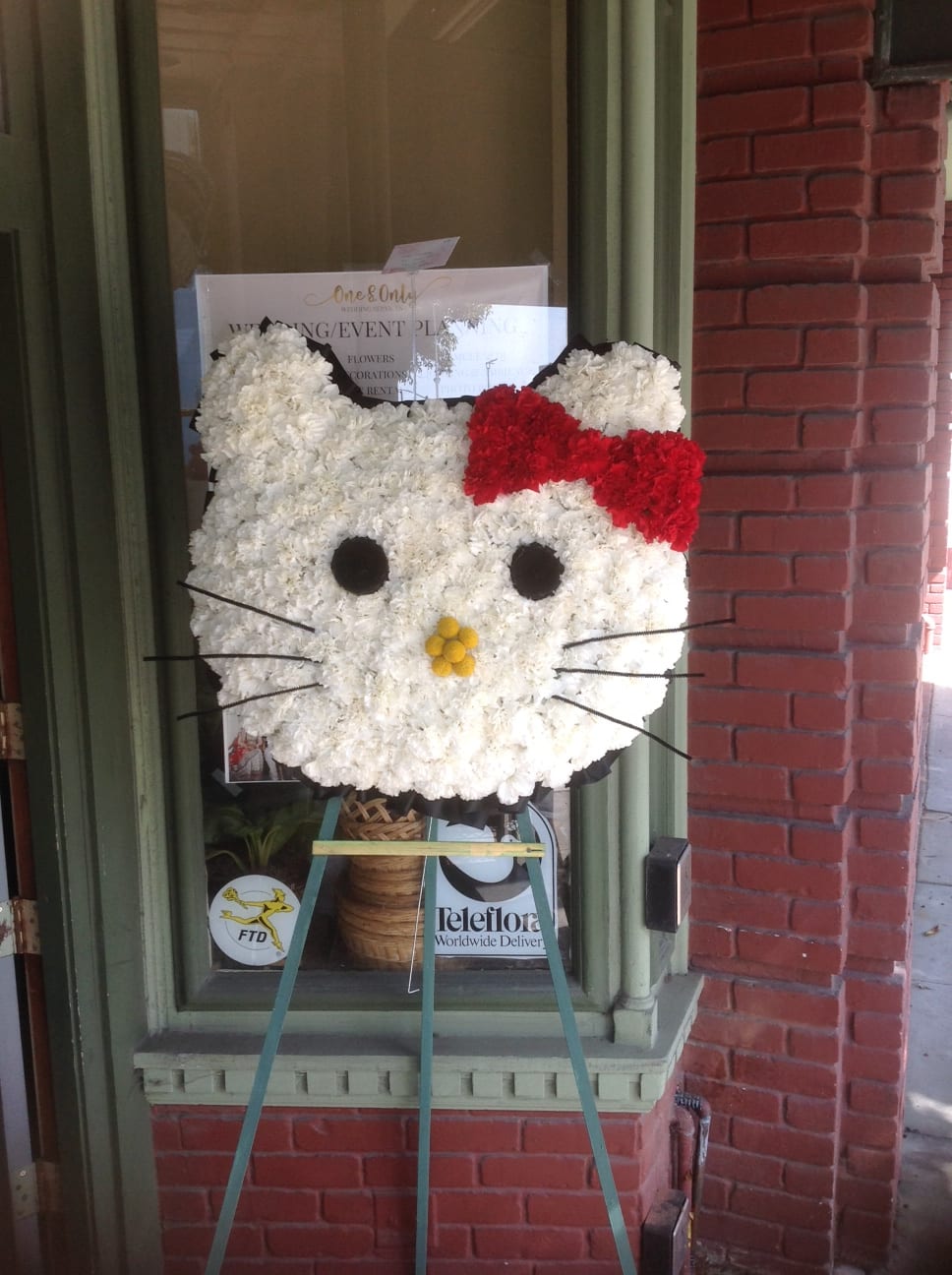 Hello Kitty-shaped floral display with a red bow on an easel