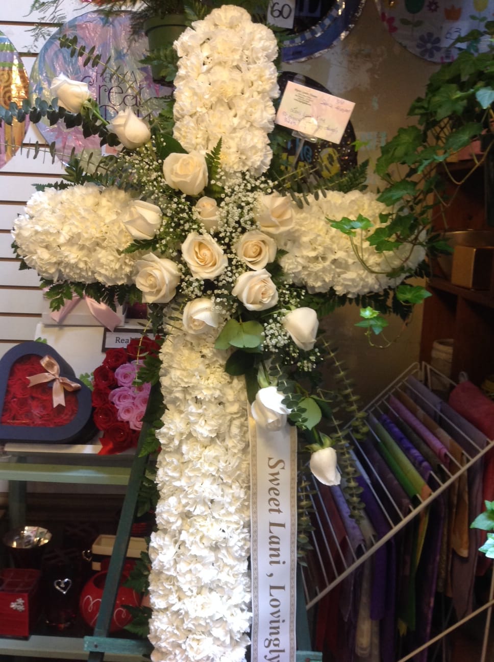 White floral cross with roses and a ribbon reading "Sweet Lani, Lovingly"
