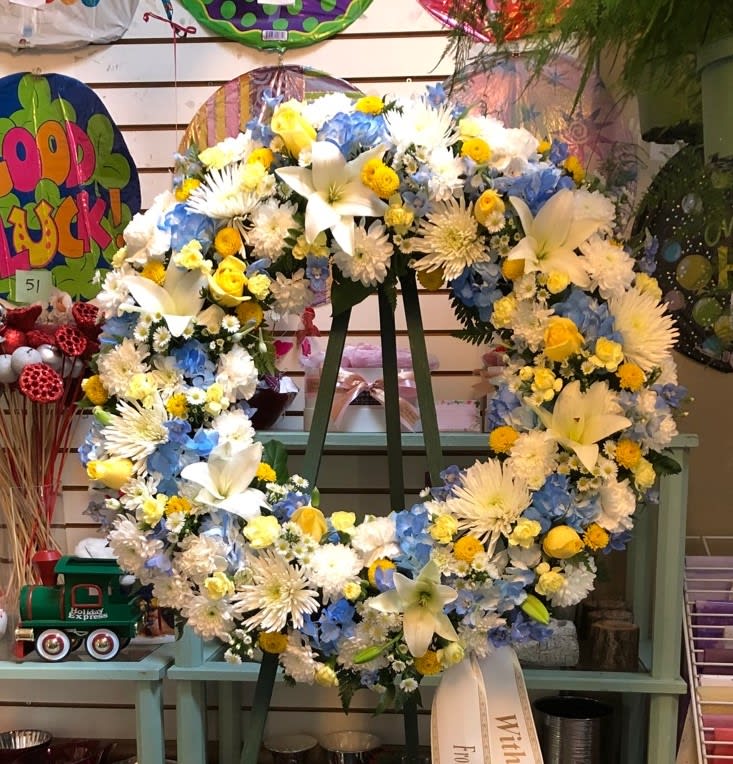 Large floral wreath with white lilies, blue hydrangeas, and yellow accents on an easel