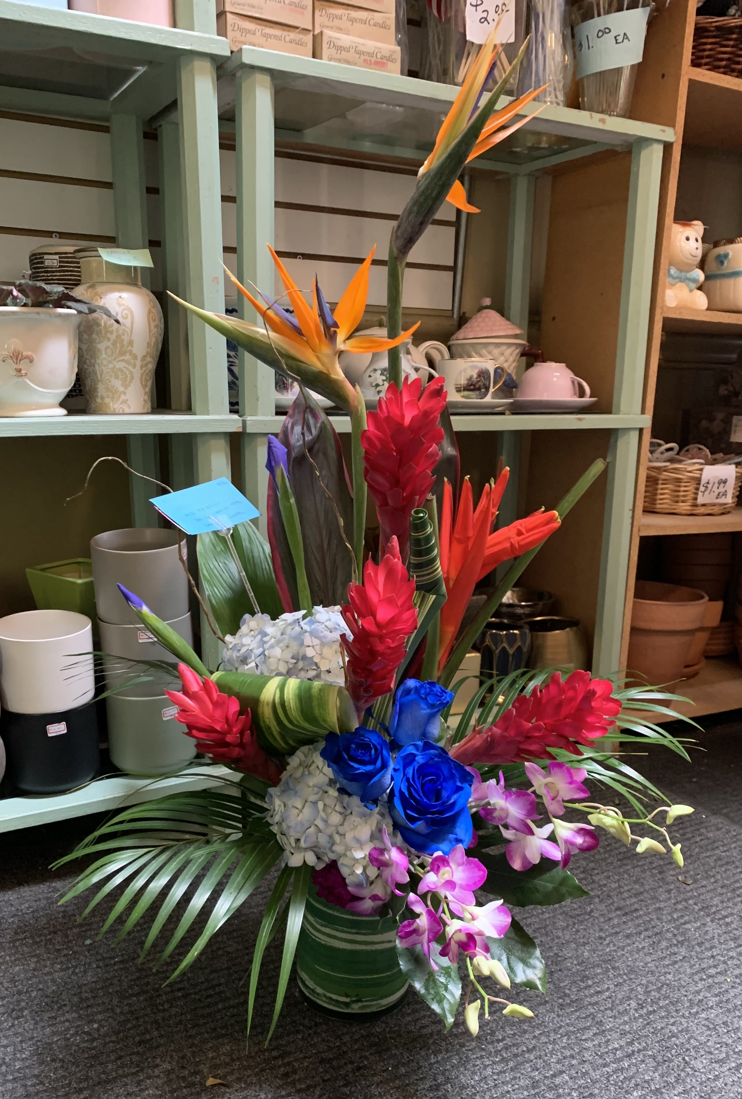 Tropical arrangement with bird of paradise, blue roses, orchids, and red ginger in a vase