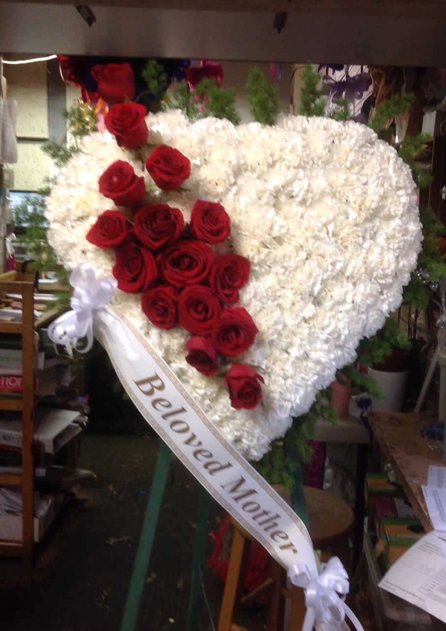 Heart-shaped white floral wreath with red roses and a ribbon