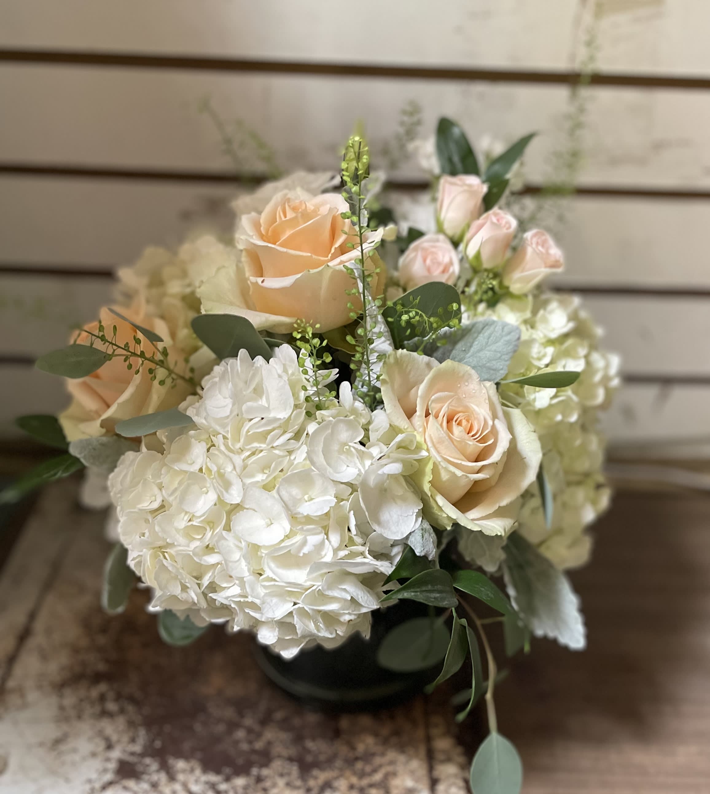 Low round arrangement of peach roses and white hydrangeas in a glass vase