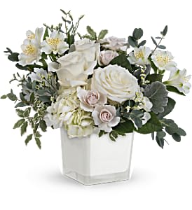 White floral arrangement in a square white vase with greenery