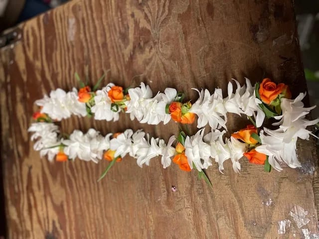 Two white and orange flower garlands laid on a wooden surface