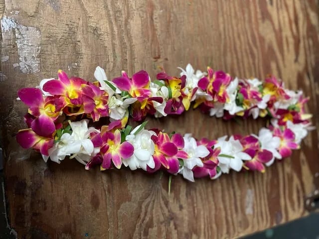 Two floral leis made of pink, yellow, and white orchids on a wooden surface