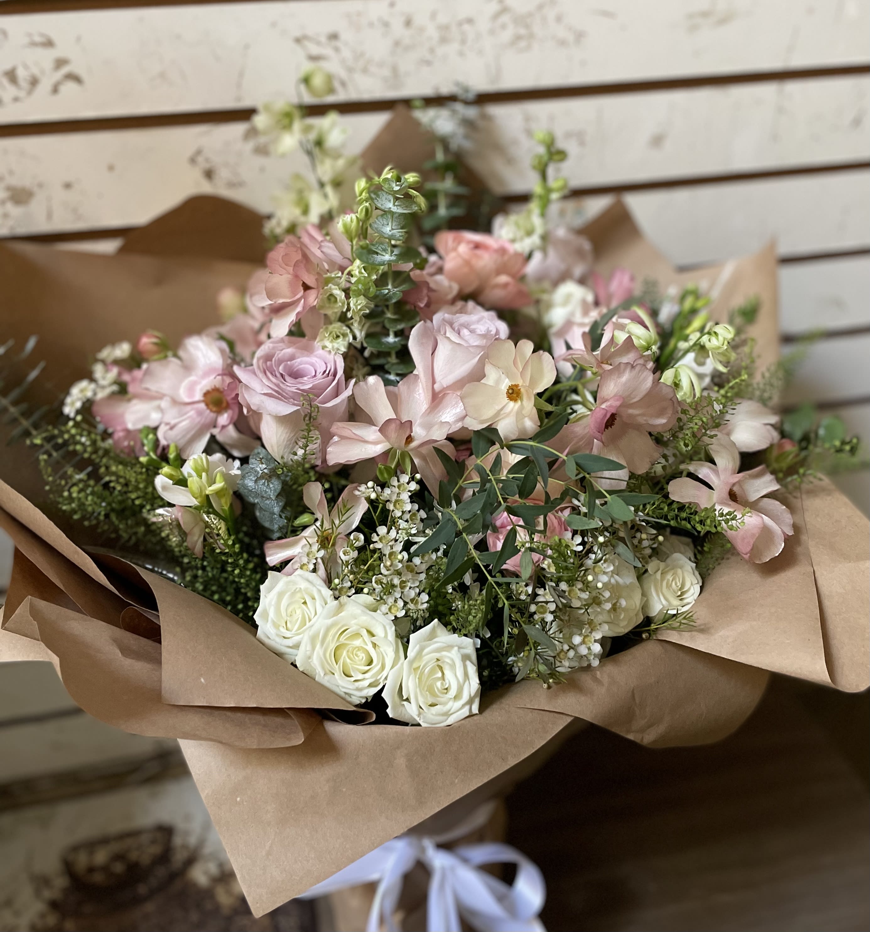 Bouquet of blush and white roses with pale pink flowers in brown paper