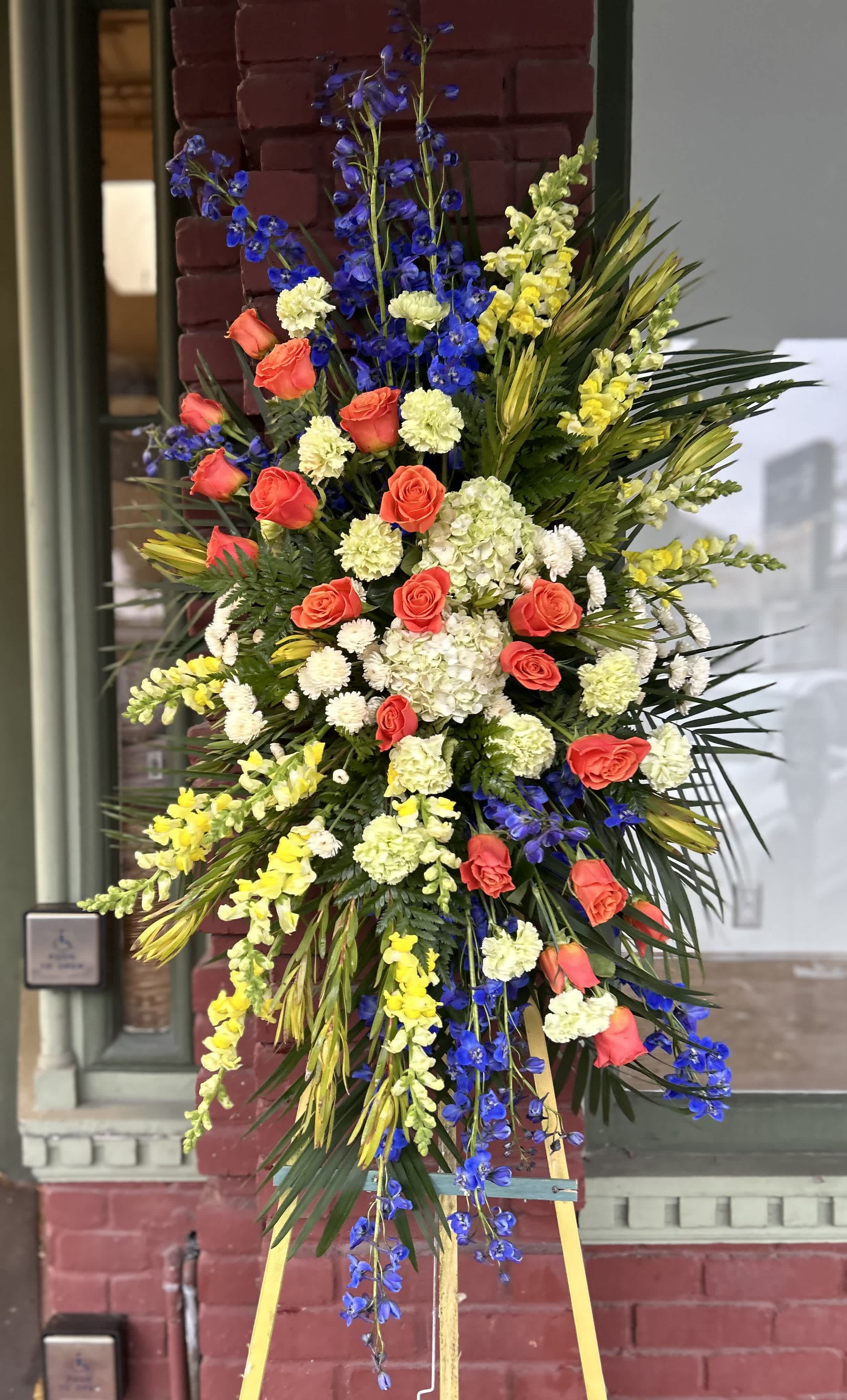 Standing floral spray with red roses, blue delphinium, and yellow snapdragons