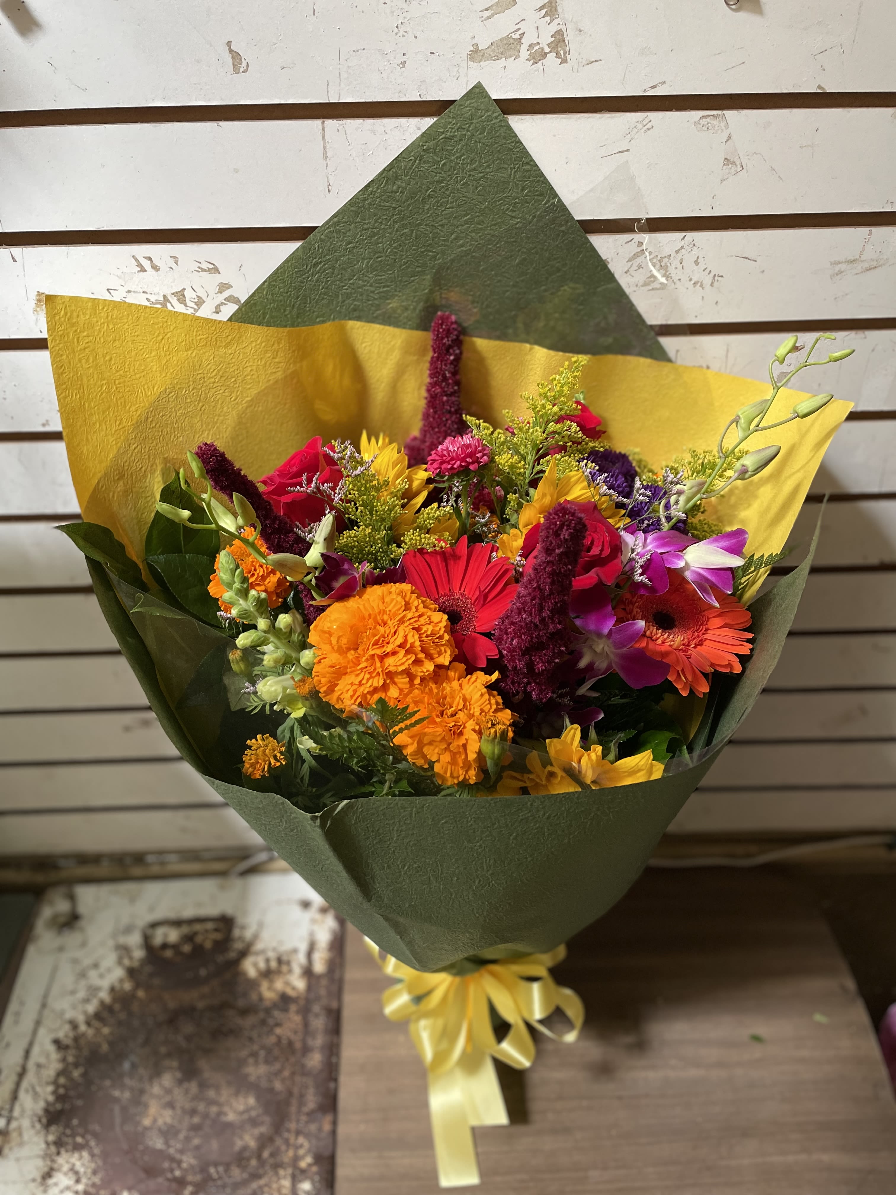 Colorful mixed bouquet wrapped in green and yellow paper with a ribbon