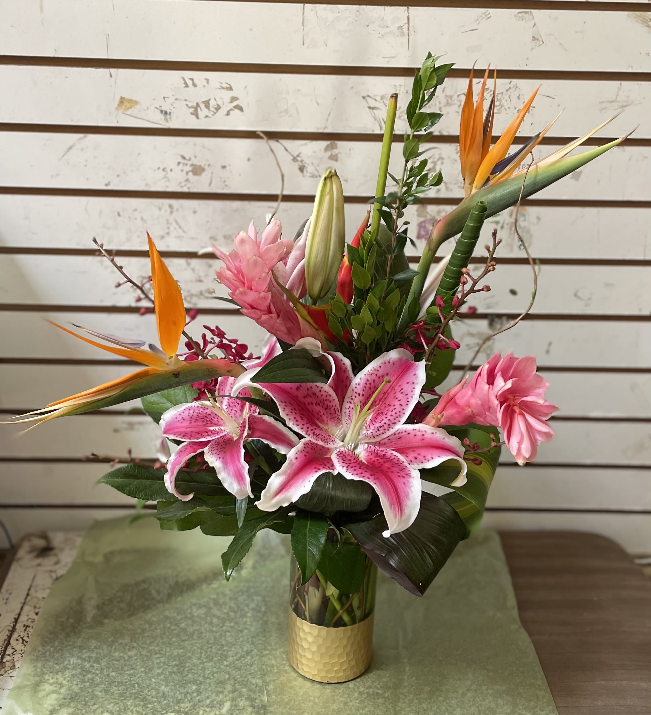 Tall tropical arrangement with pink lilies and orange bird of paradise in a gold vase