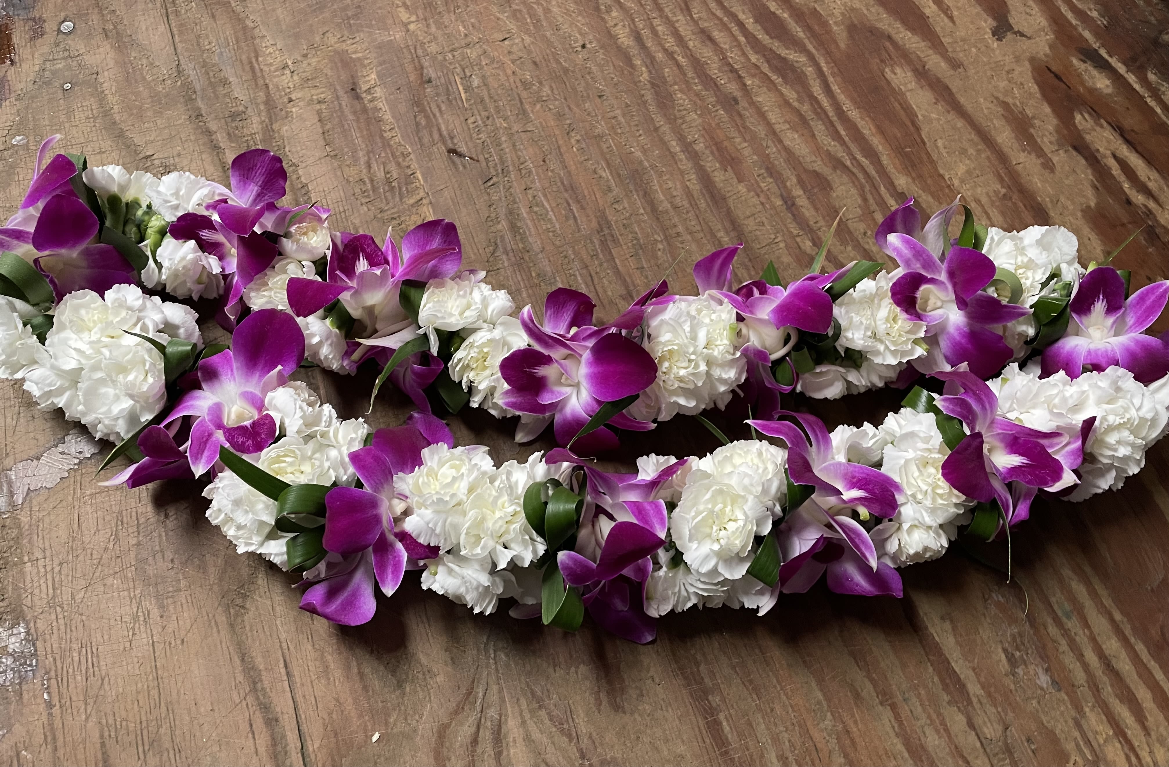 Purple orchid and white carnation floral garlands on a wooden surface