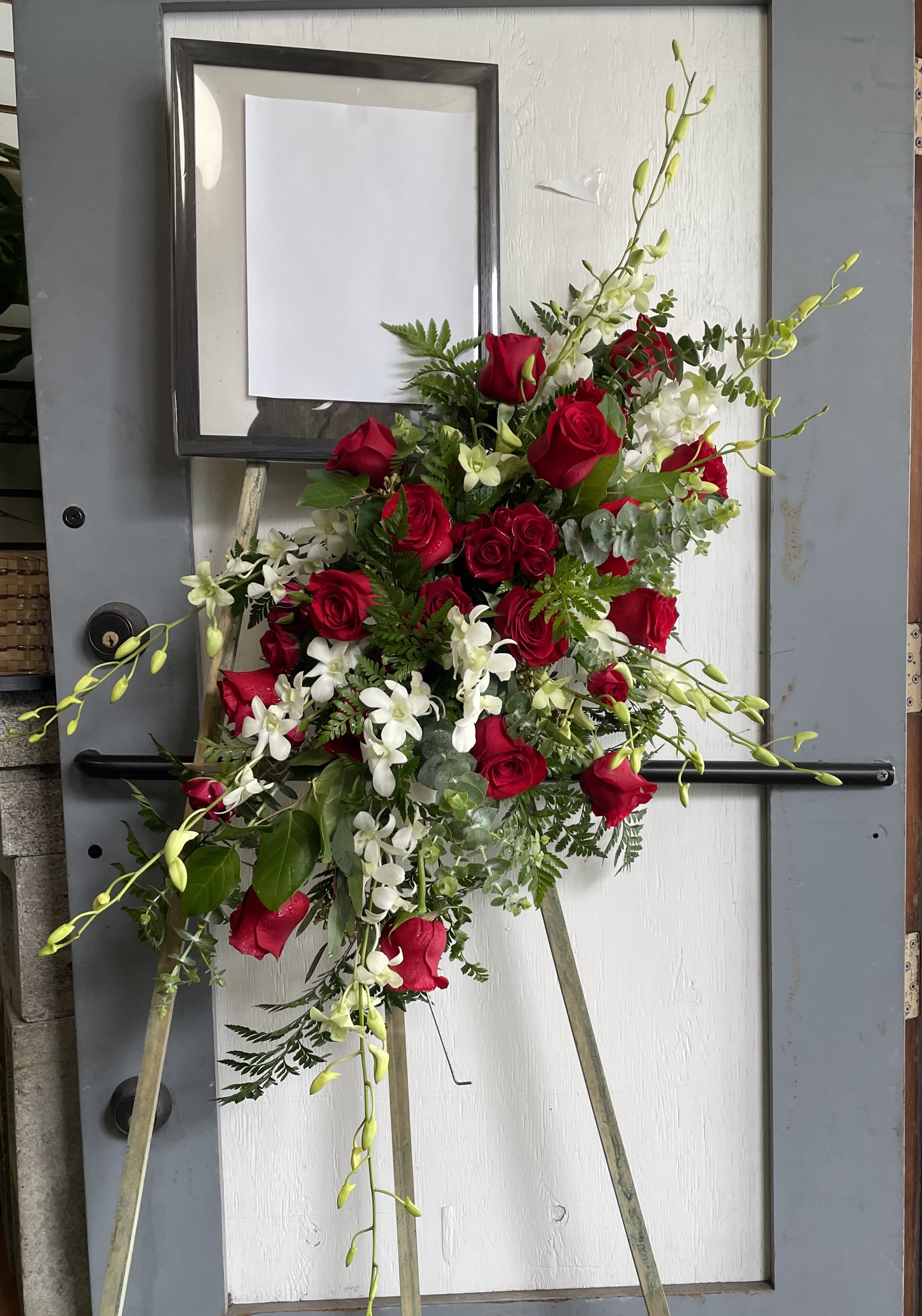 Standing floral spray with red roses and white orchids on an easel