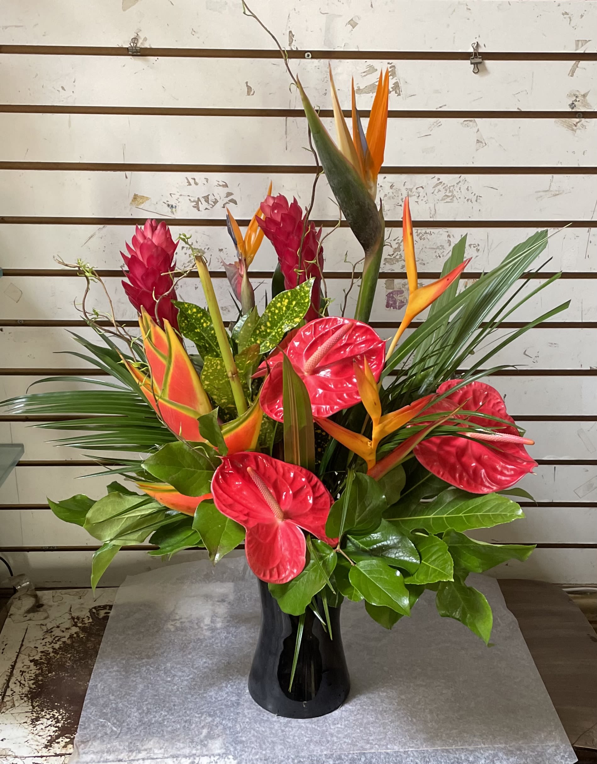 Tall tropical arrangement with red anthurium and orange bird-of-paradise in a black vase