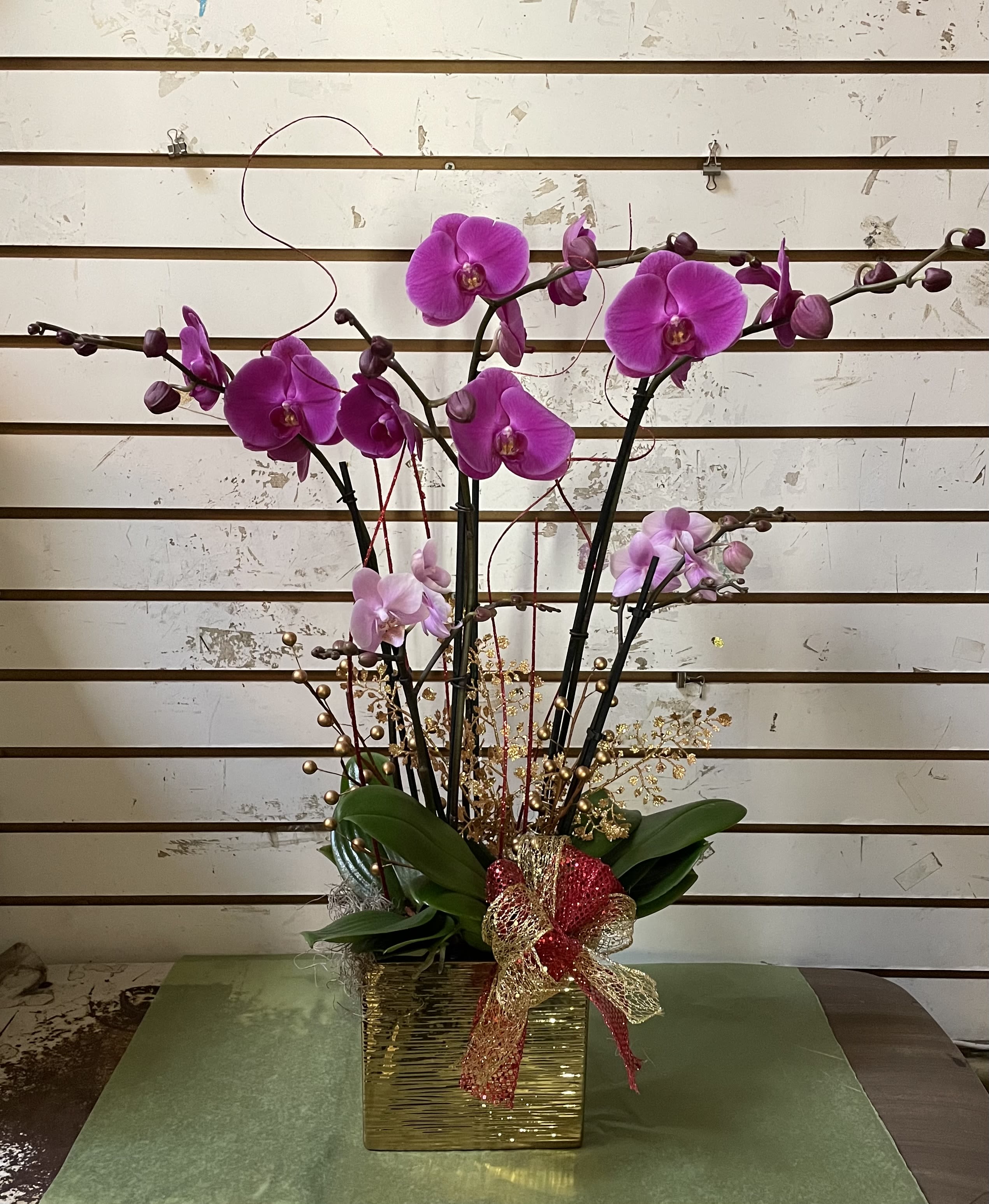 Pink orchid arrangement in a gold square vase with a decorative bow