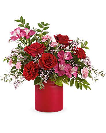 Arrangement of red roses, red carnations, and pink flowers in a matte red cylinder vase