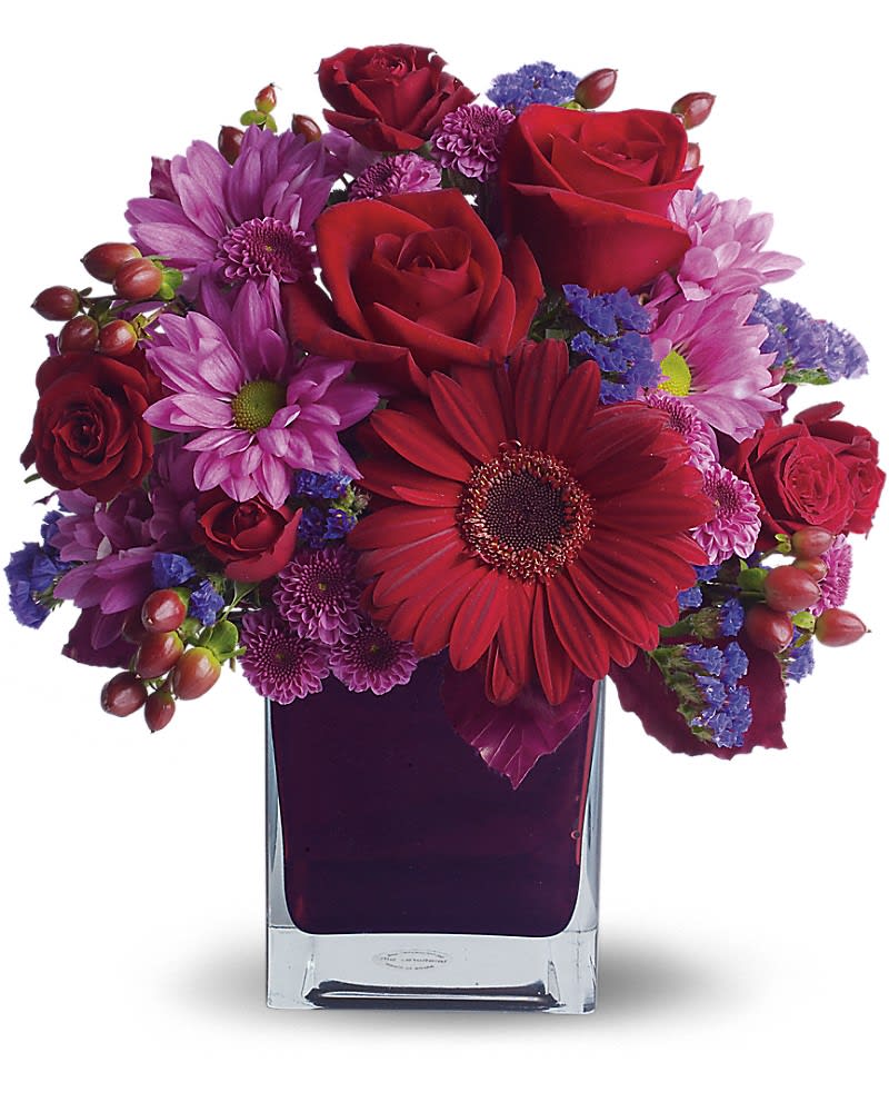 Red roses and purple daisies arranged in a square glass vase