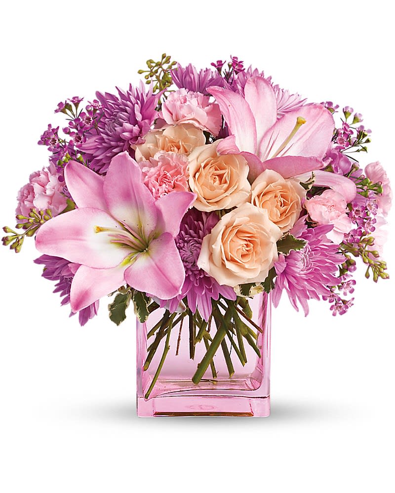 Pink lilies, peach roses, and mixed pink flowers arranged in a pink glass rectangular vase