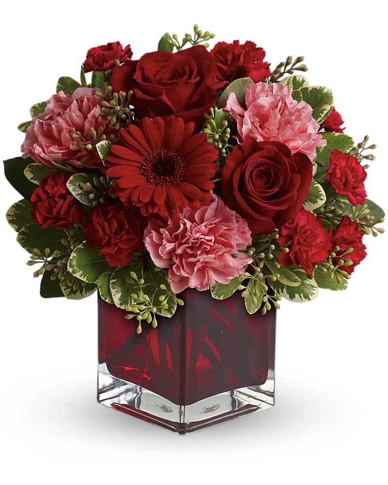 Red and pink roses, carnations, and a gerbera daisy arranged in a red glass cube vase