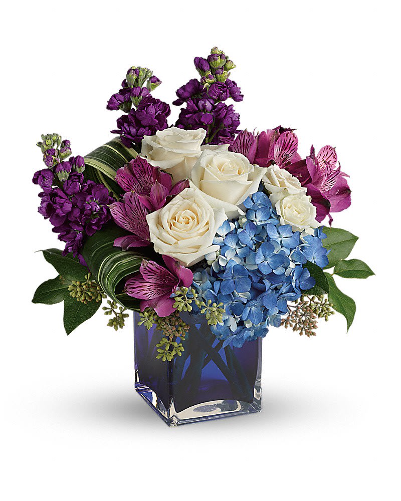 Bouquet of white roses, blue hydrangeas, and purple flowers in a blue glass vase