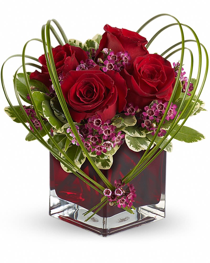 Red roses and purple filler flowers in a square glass vase
