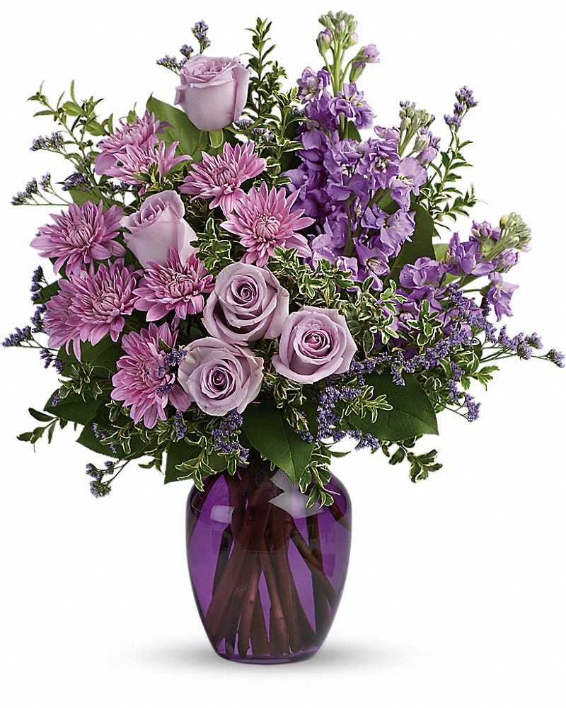 Lavender roses and purple mums arranged with filler flowers in a purple glass vase