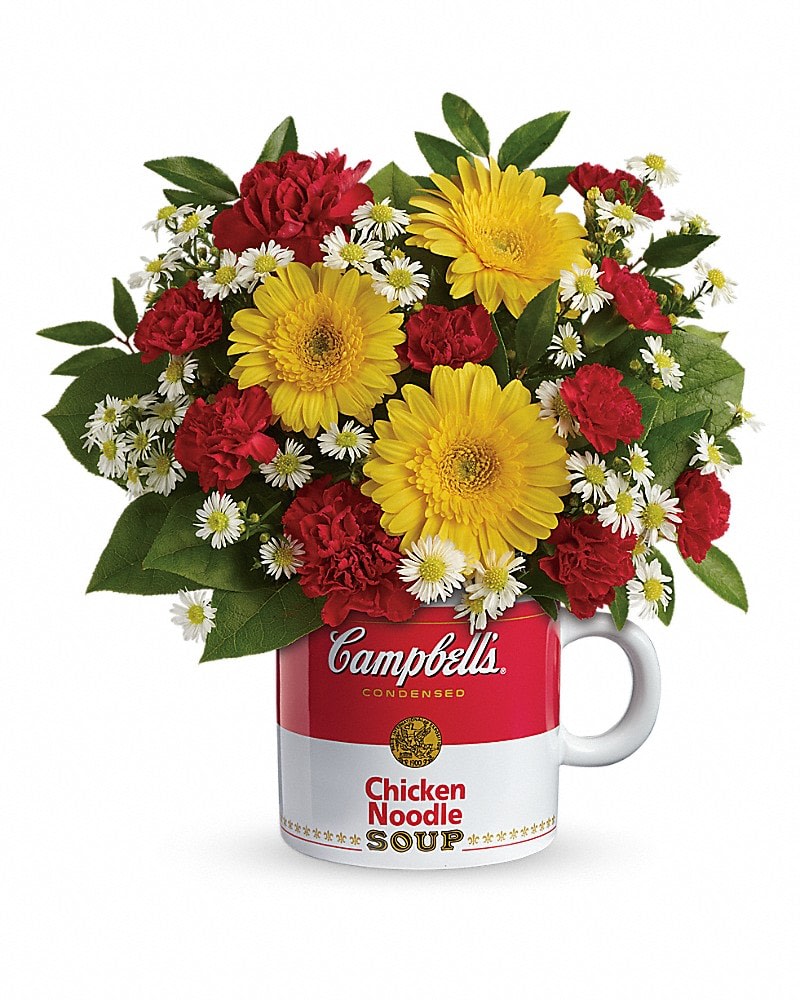 Yellow gerbera daisies, red carnations, and small white daisies in a Campbell's soup mug.
