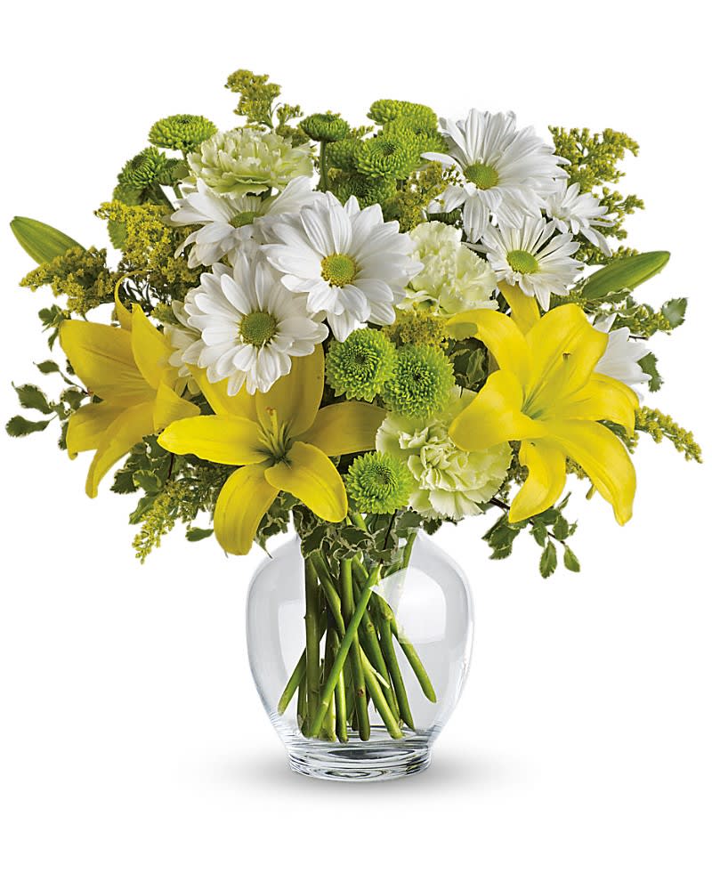 Yellow lilies with white daisies and green flowers arranged in a clear glass vase