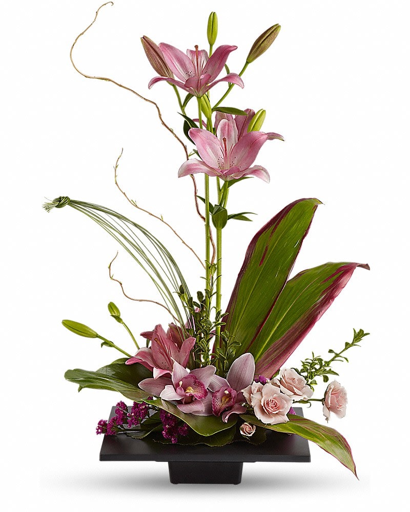 Pink lilies and orchids arranged in a black vase with tropical leaves