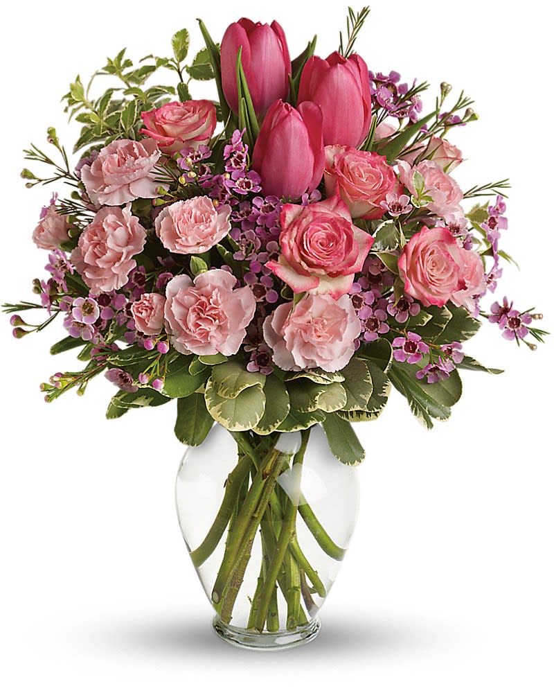 Pink tulips, roses, carnations, and small purple blossoms arranged in a clear glass vase