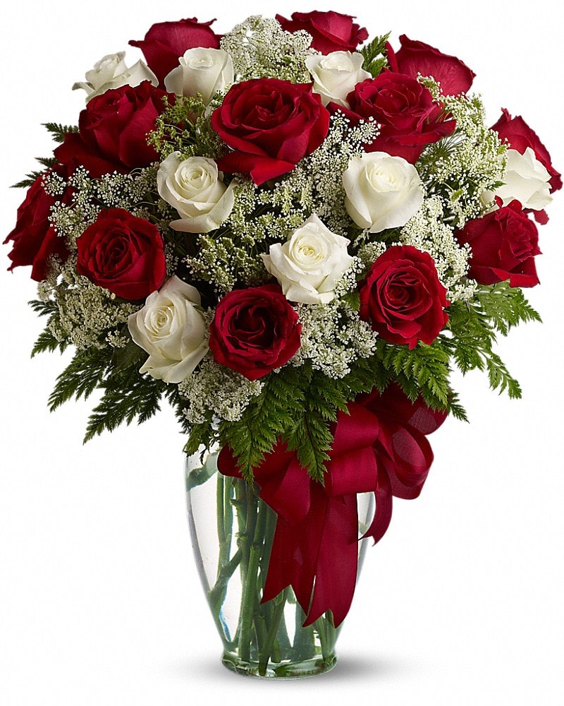 Red and white roses arranged in a clear glass vase with a red ribbon