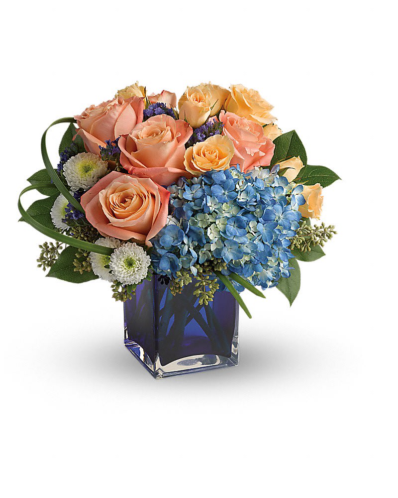 Peach roses and blue hydrangeas in a square glass vase