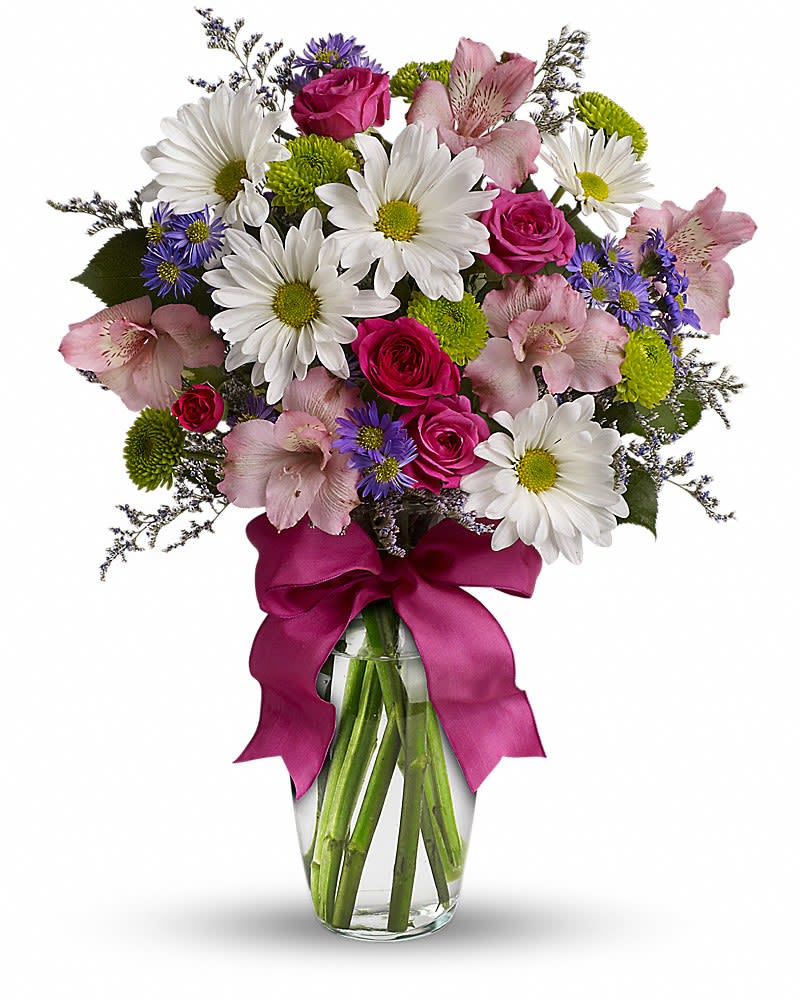 Mixed bouquet of white daisies, pink roses, and purple asters in a clear vase with a magenta bow