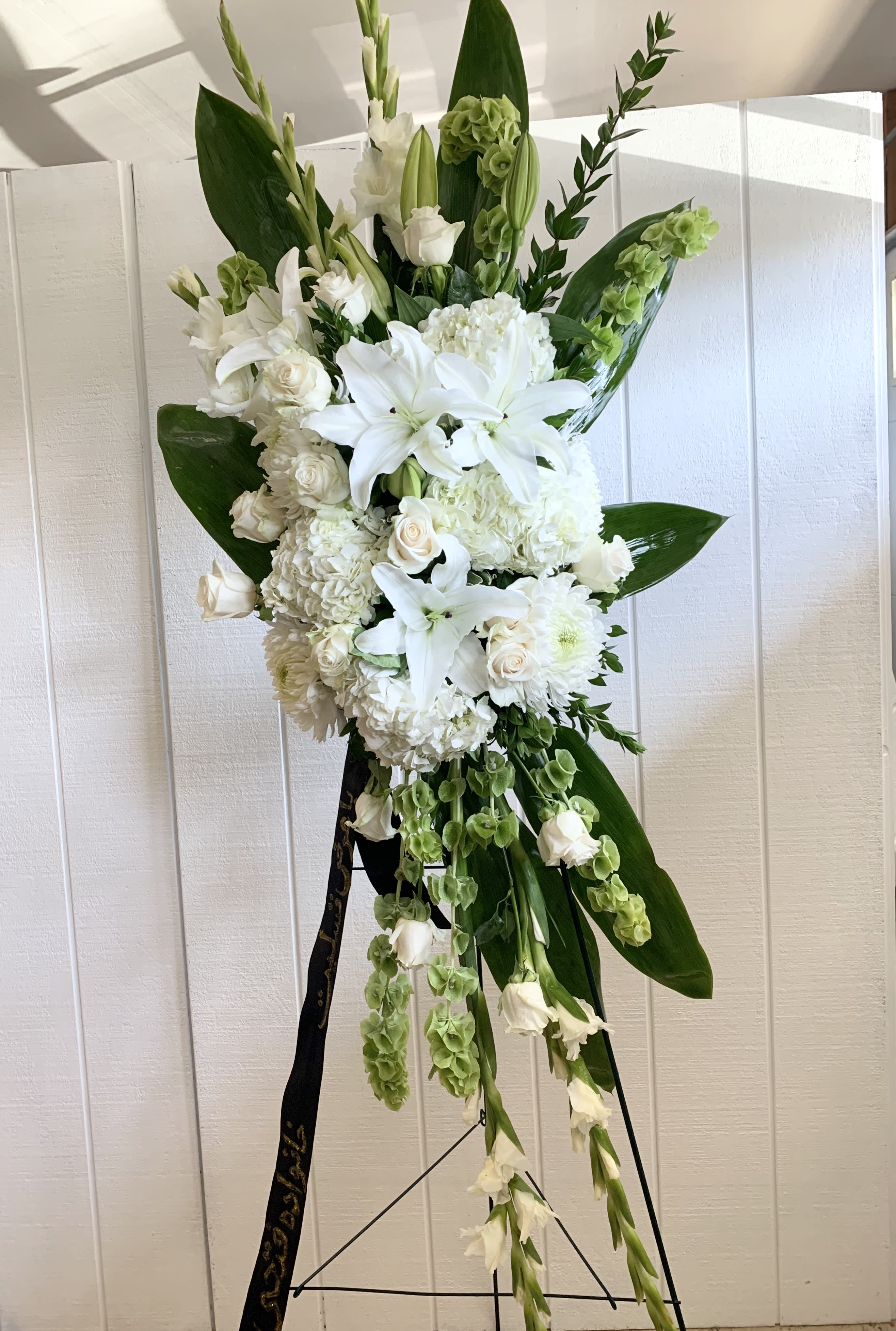 Tall white floral standing spray on an easel with lilies and roses