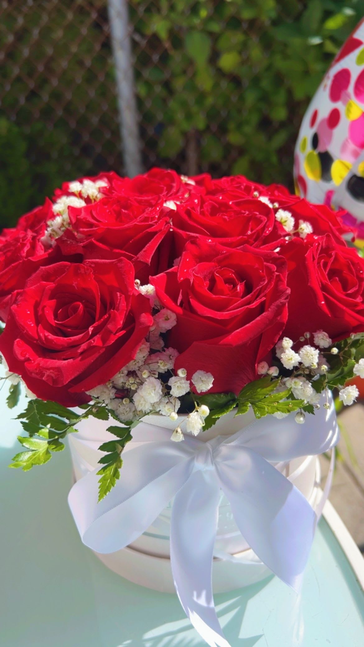 Red roses arranged in a white hat box with baby's breath and a white ribbon