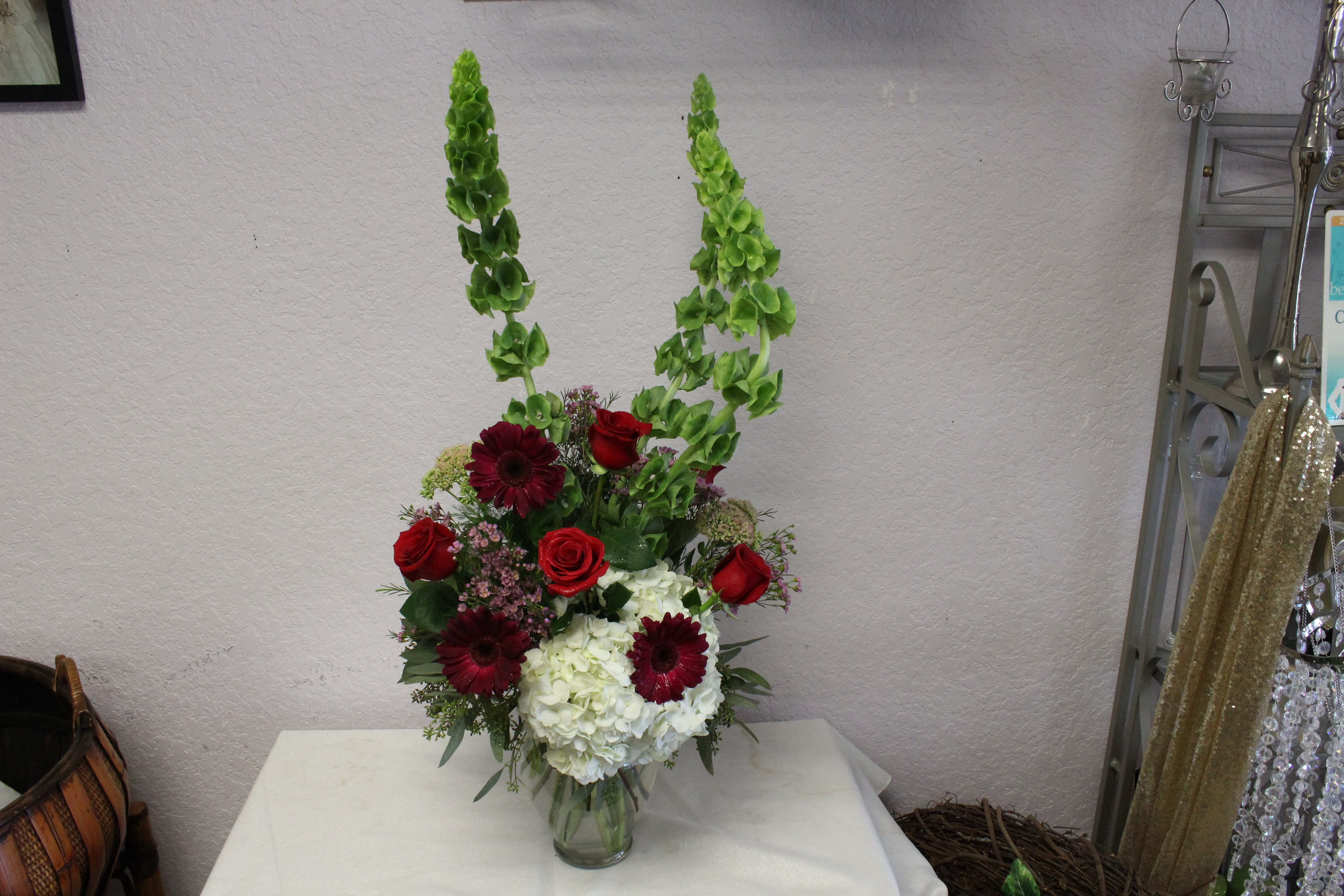 Tall floral arrangement with red roses, burgundy daisies, and white hydrangeas in a glass vase
