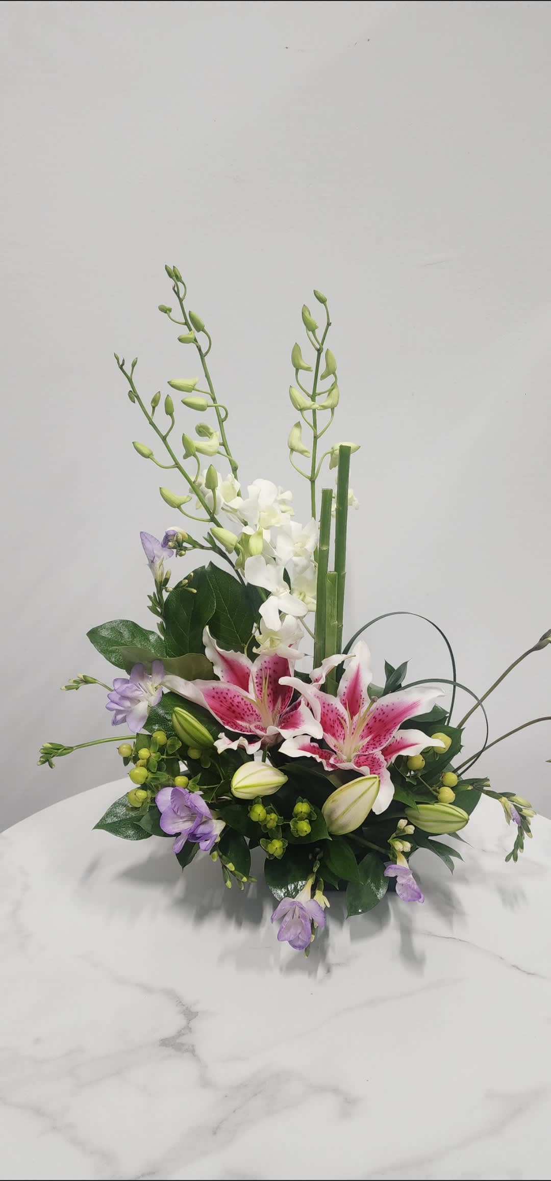 Pink stargazer lilies and purple flowers in a low floral arrangement
