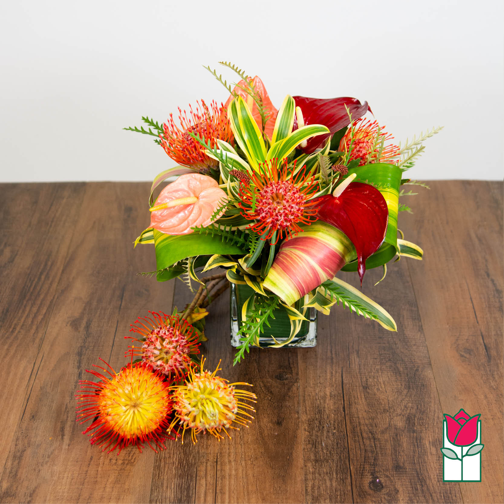 Tropical bouquet in a square glass vase with red and peach blooms