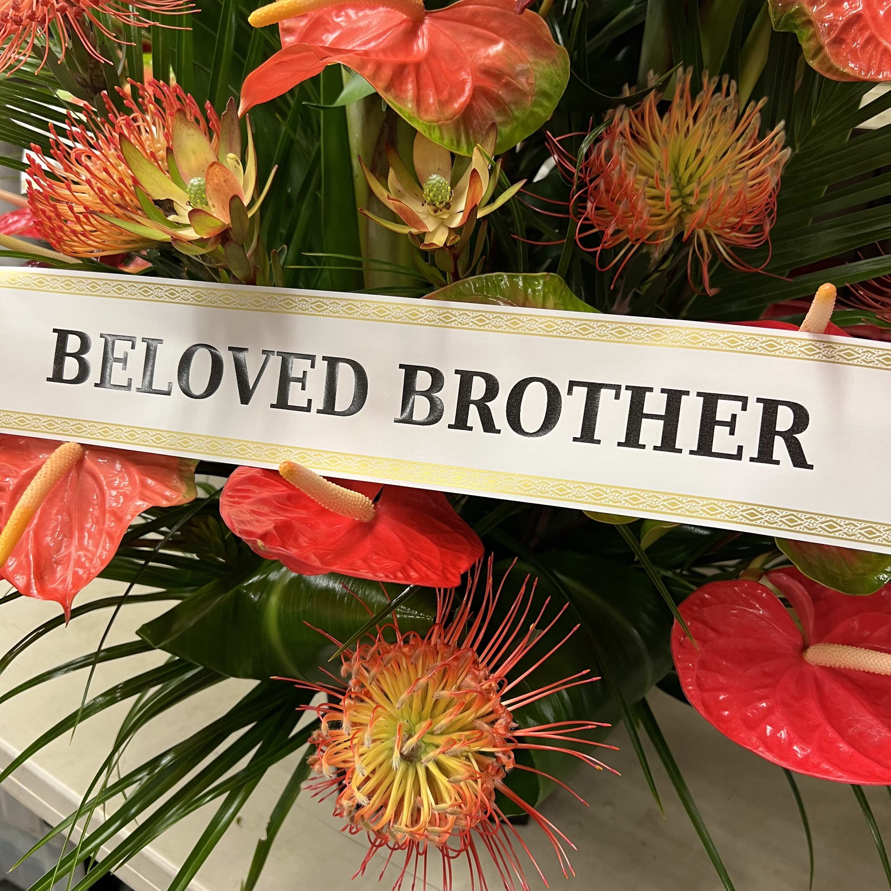 Tropical floral tribute with red anthuriums and orange protea, labeled beloved brother