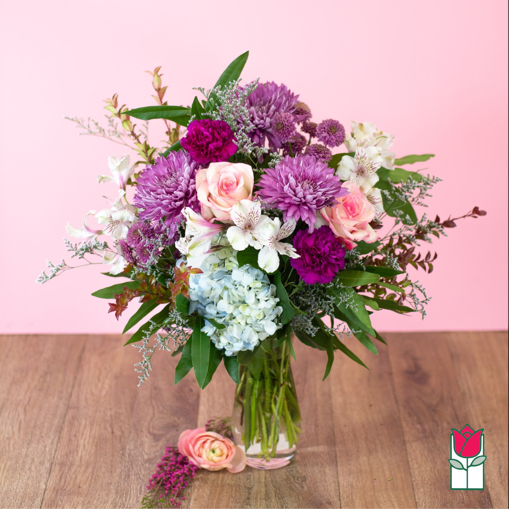 Mixed pink, purple, and white flower arrangement with hydrangea in a clear glass vase