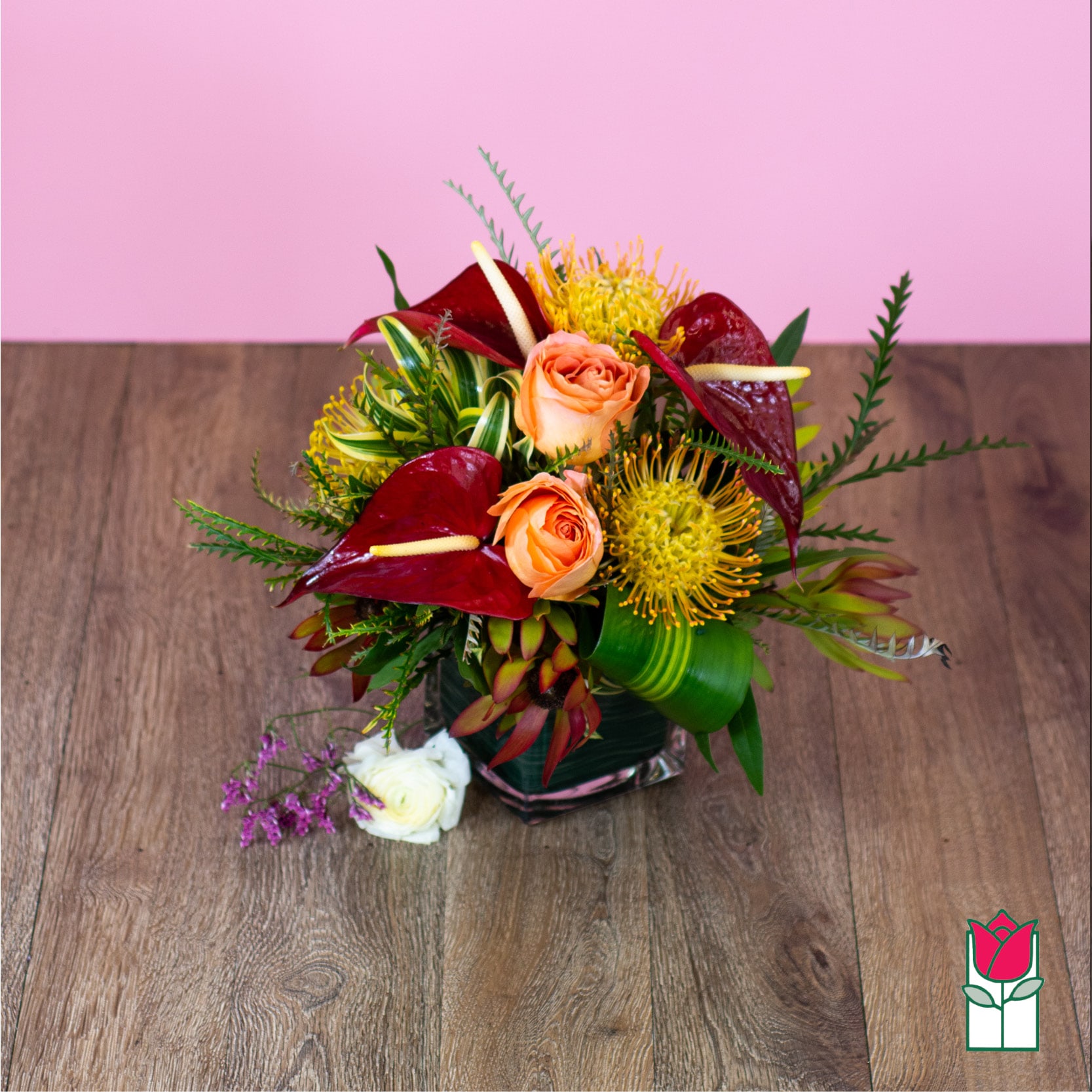 Tropical bouquet with peach roses and red anthuriums in a glass vase