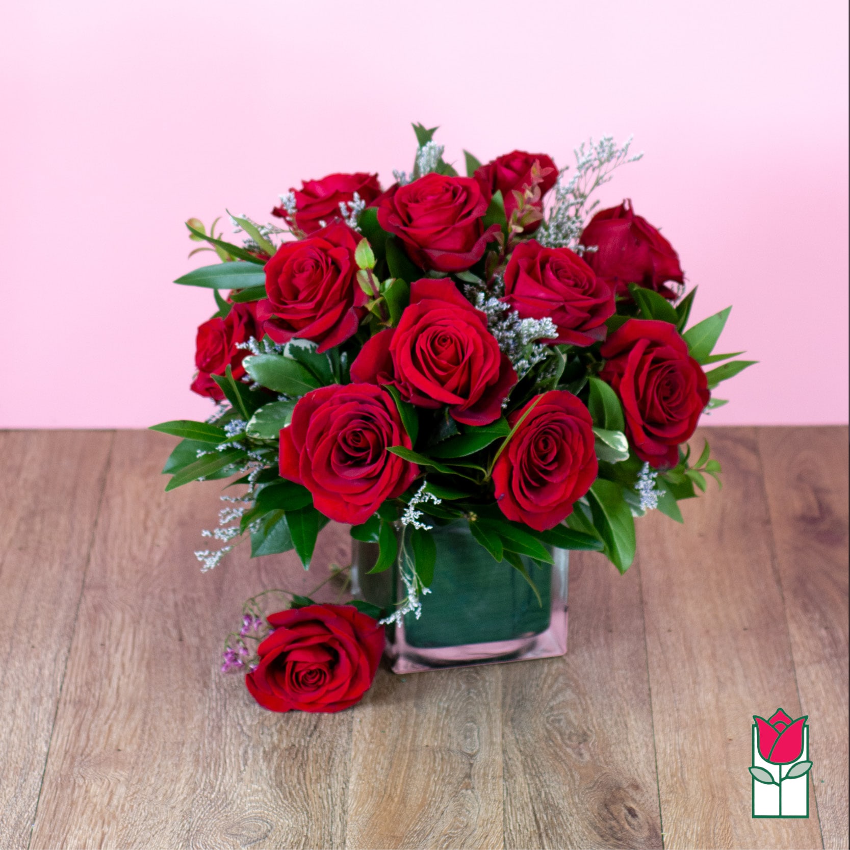 Red rose bouquet in a square glass vase on a wooden surface