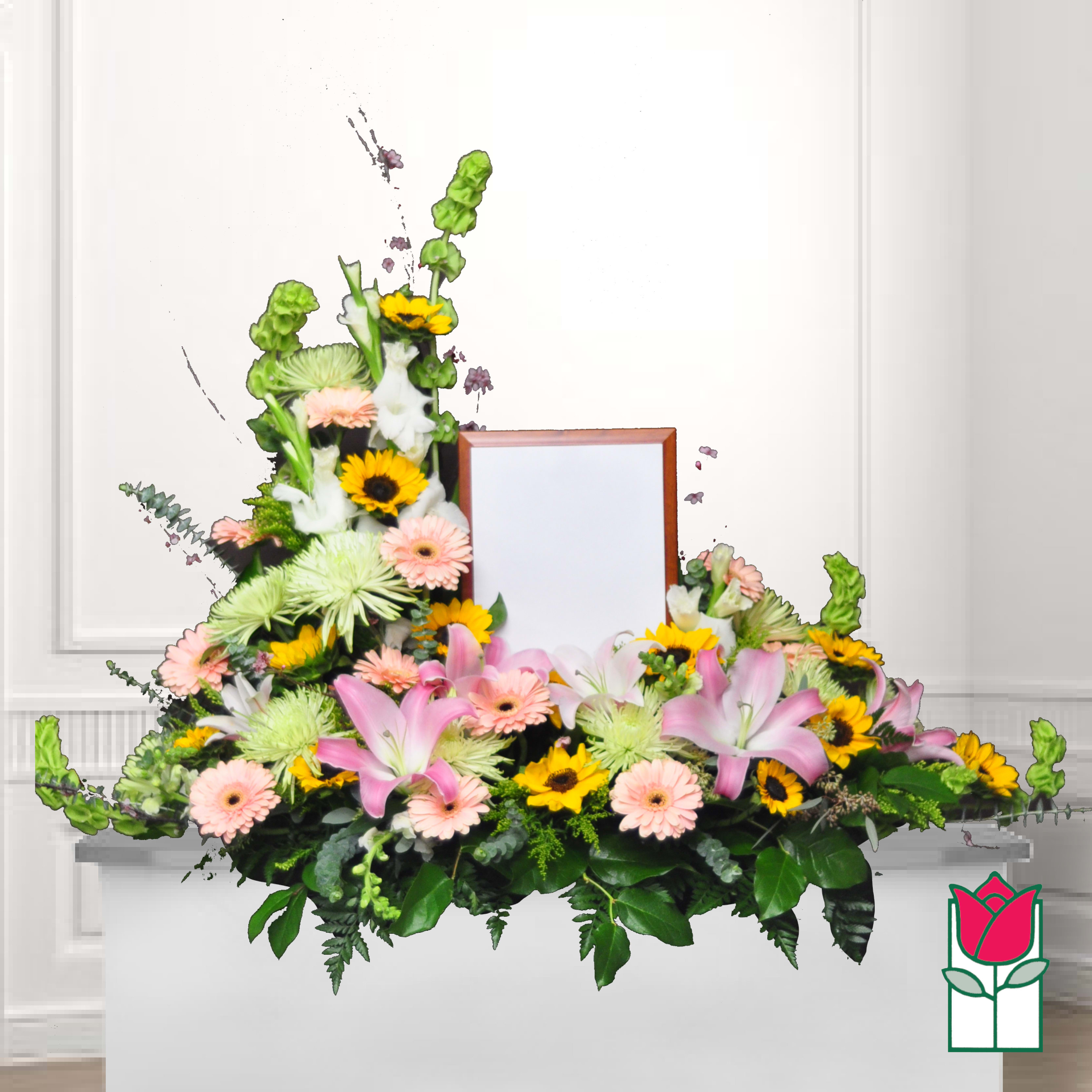 Symmetrical floral funeral spray with pink lilies, daisies, and sunflowers around a framed center