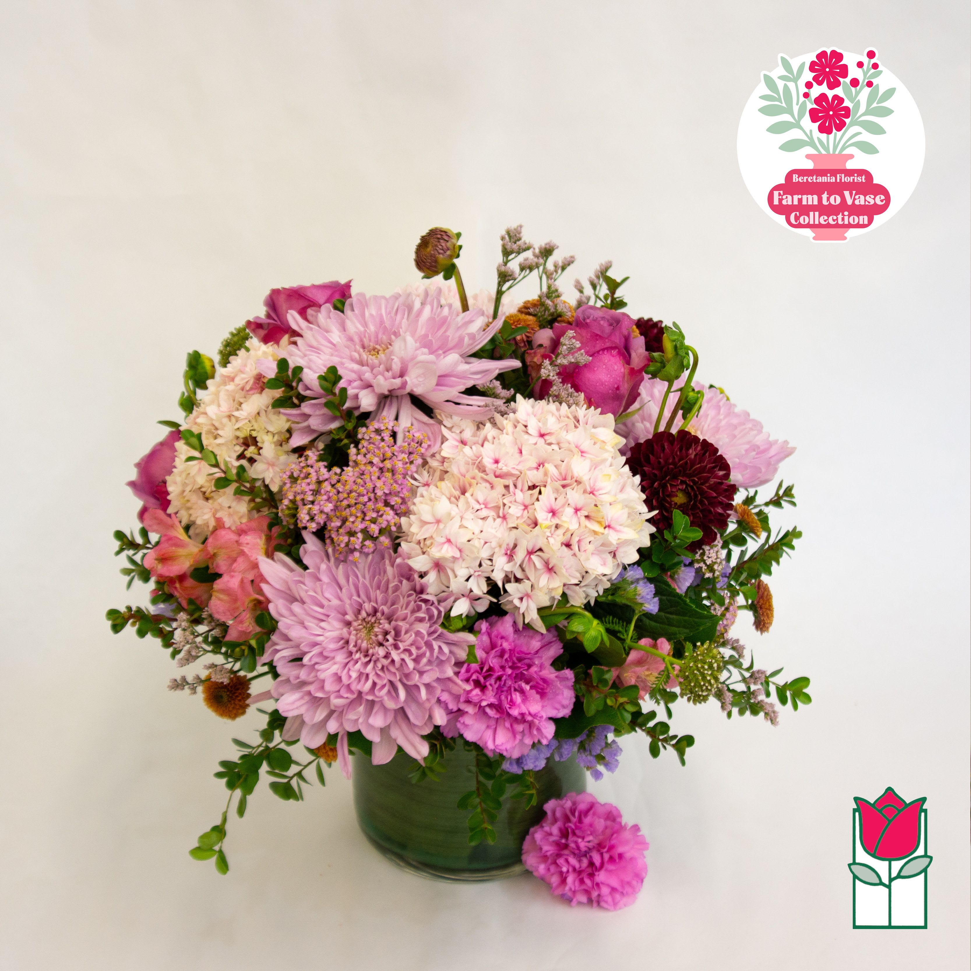 Mixed pink and purple flower arrangement in a green glass vase