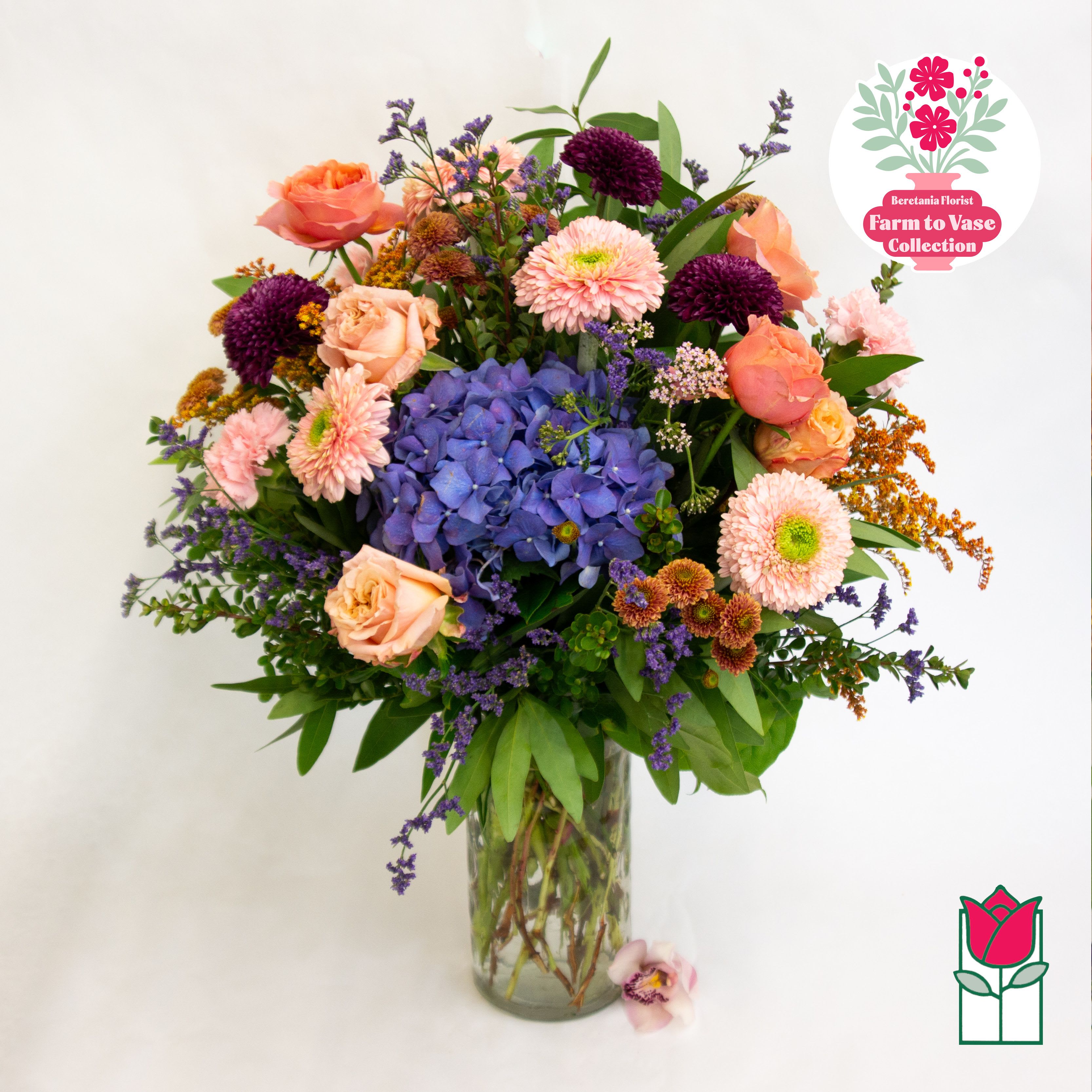 Mixed bouquet of peach roses, blue hydrangea, and pink blooms in a glass vase