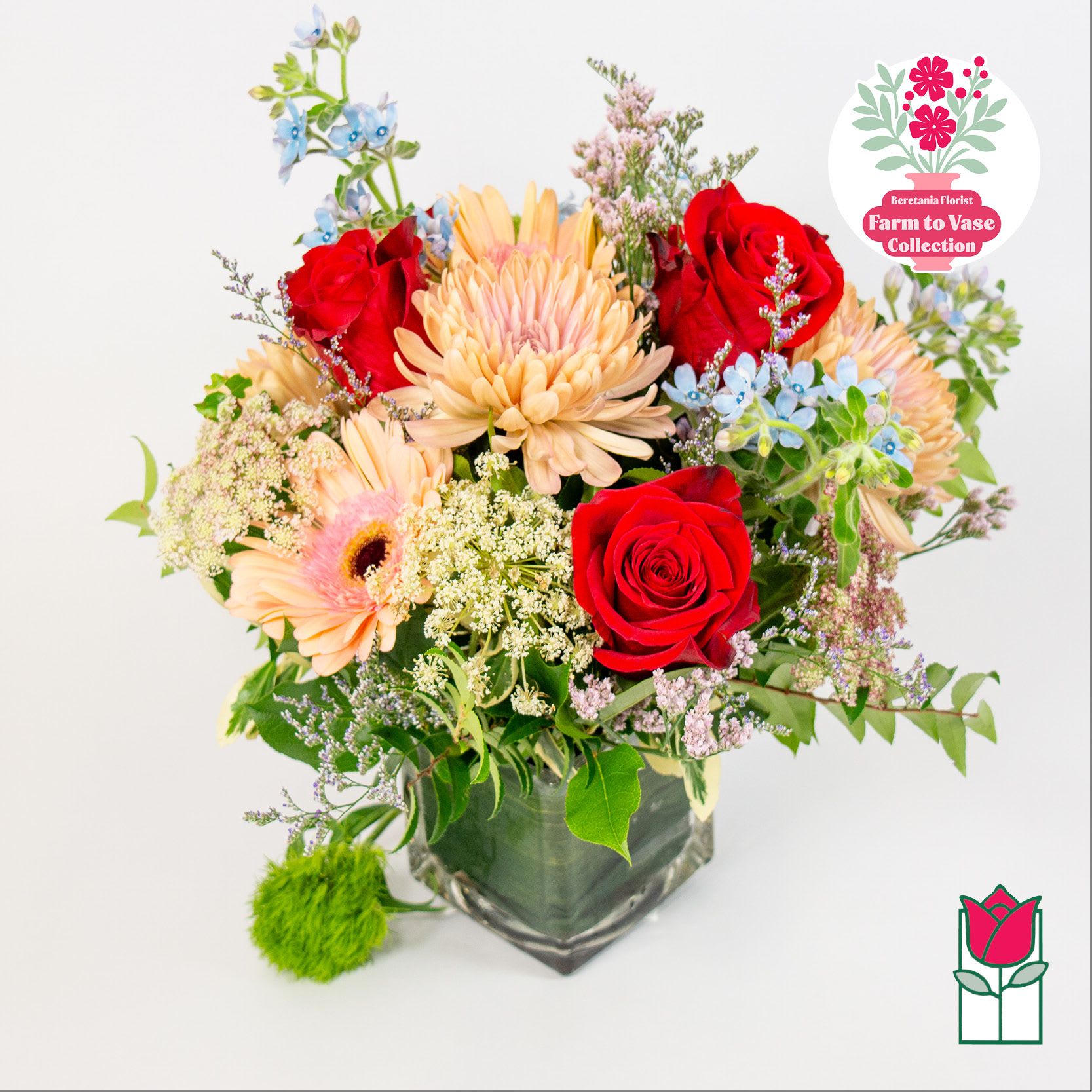 Mixed bouquet of red roses, peach daisies, and blue flowers in a glass vase